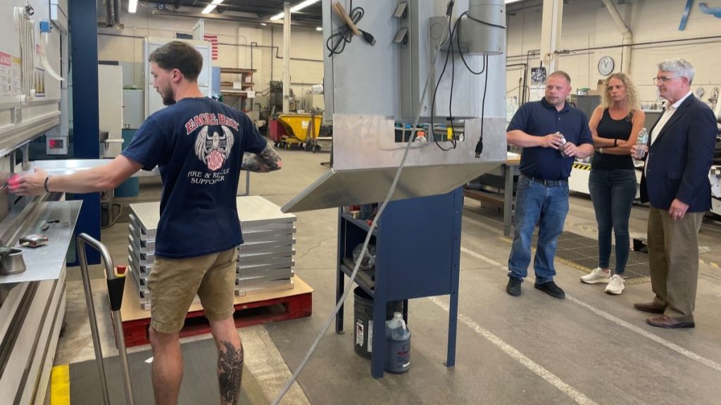 Team member Alan operates a machine as fellow team members Jim and Erin give Congressman a tour of Eagle Metalcraft.