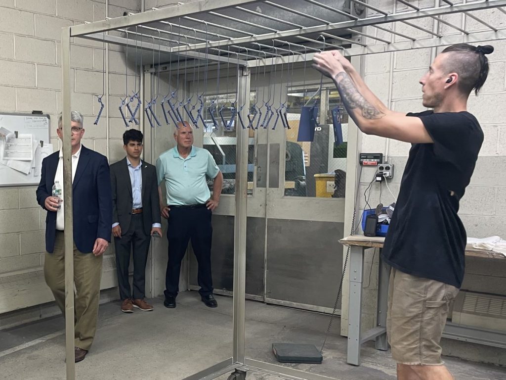 Team member Sean hangs products to dry as Congressman Williams tours the facility.